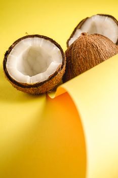 Coconut fruits on folded paper yellow plain background, abstract food tropical concept, angle view