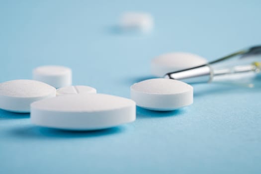 Pills, tablets and analog thermometer on bright blue background, healthcare medical concept, antibiotics and cure, angle view macro