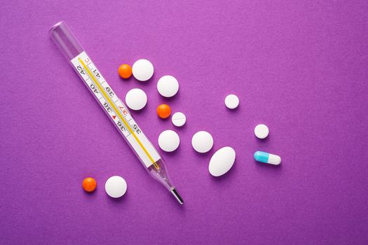 Pills, tablets and analog thermometer on violet purple background, healthcare medical concept, antibiotics and cure, top view copy space