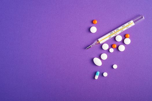 Pills, tablets and analog thermometer on violet purple background, healthcare medical concept, antibiotics and cure, top view copy space