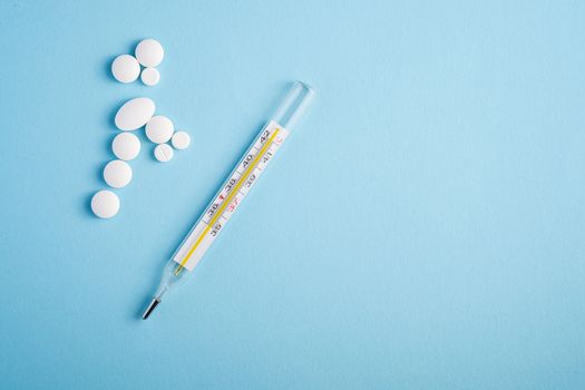 Pills, tablets and analog thermometer on bright blue background, healthcare medical concept, antibiotics and cure, top view copy space