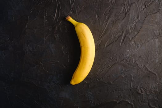 Single banana fruit on dark textured background, top view copy space