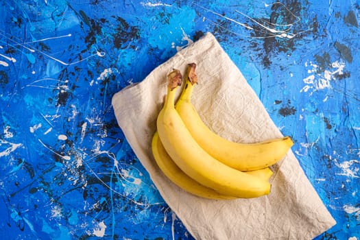 Banana fruits with tablecloth on blue textured background, top view copy space