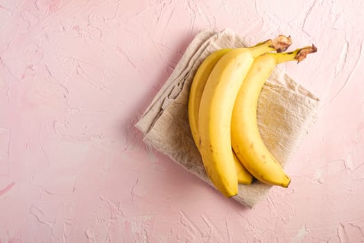 Banana fruits with tablecloth on pink textured background, top view copy space