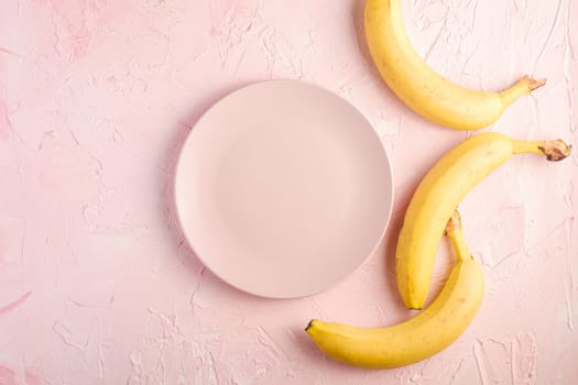 Banana fruits with empty pink plate on pink textured background, top view copy space