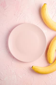 Banana fruits with empty pink plate on pink textured background, top view copy space