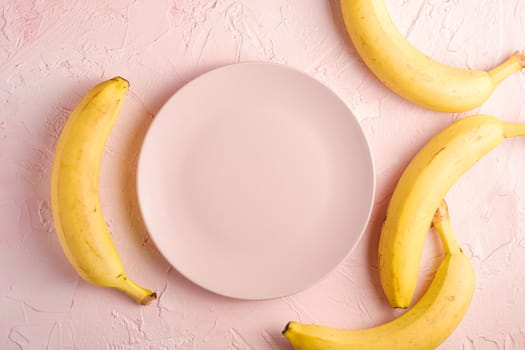 Banana fruits with empty pink plate on pink textured background, top view copy space