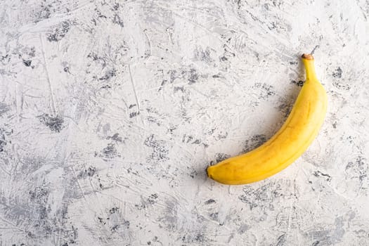 Single banana fruit on white textured background, top view copy space