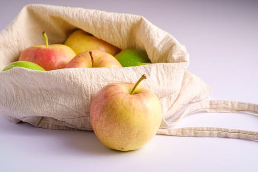 Fresh sweet apples in reusable textile grocery bag on white background, angle view macro