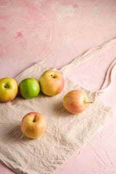 Fresh sweet apples on reusable textile grocery bag on pink textured background, angle view