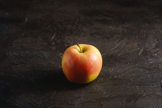 Fresh sweet single apple on dark black textured background, angle view