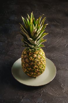 Fresh sweet pineapple in grey plate on dark black textured background, angle view