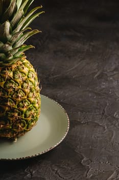 Fresh sweet pineapple in grey plate on dark black textured background, angle view, cropped