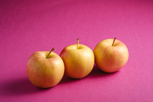 Fresh sweet three apples on pink purple textured background, angle view