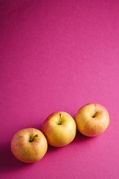 Fresh sweet three apples on pink purple textured background, angle view copy space