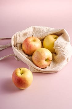 Fresh sweet apples in reusable textile grocery bag on pink background, angle view