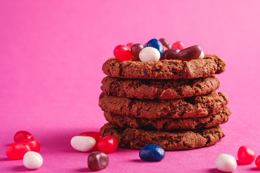 Homemade oat chocolate cookies stack with cereal with juicy jelly beans on minimal pink purple background, angle view macro