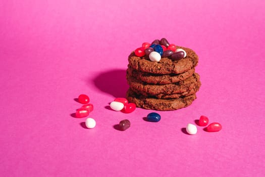 Homemade oat chocolate cookies stack with cereal with juicy jelly beans on minimal pink purple background, angle view copy space