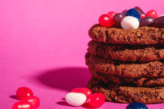 Homemade oat chocolate cookies stack with cereal with juicy jelly beans on minimal pink purple background, angle view macro