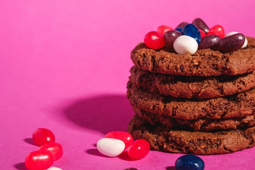 Homemade oat chocolate cookies stack with cereal with juicy jelly beans on minimal pink purple background, angle view macro