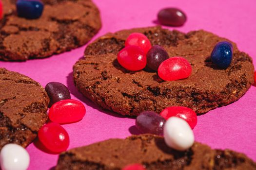 Homemade oat chocolate cookies with cereal with juicy jelly beans on minimal pink purple background, angle view macro