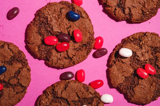 Homemade oat chocolate cookies with cereal with juicy jelly beans on minimal pink purple background, top view macro