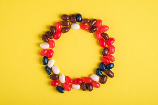 Round frame of juicy sweet fruit colorful jelly beans on bright yellow background, top view copy space