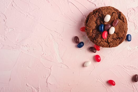 Homemade oat chocolate cookies stack with cereal with juicy jelly beans on textured pink background, top view copy space