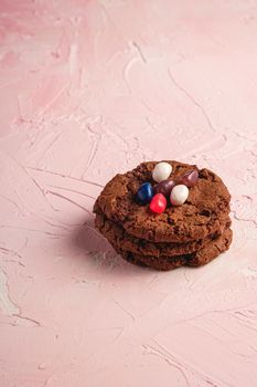 Homemade oat chocolate cookies stack with cereal with juicy jelly beans on textured pink background, angle view