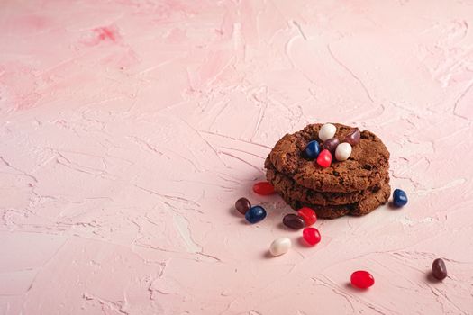 Homemade oat chocolate cookies stack with cereal with juicy jelly beans on textured pink background, angle view copy space