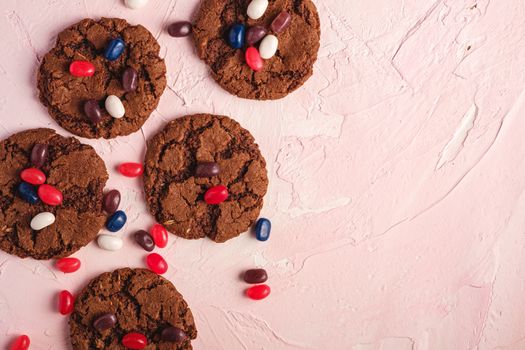 Homemade oat chocolate cookies with cereal with juicy jelly beans on textured pink background, top view copy space