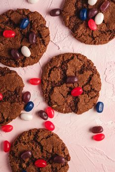 Homemade oat chocolate cookies with cereal with juicy jelly beans on textured pink background, top view