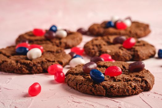 Homemade oat chocolate cookies with cereal with juicy jelly beans on textured pink background, angle view macro