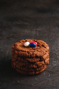 Homemade oat chocolate cookies stack with cereal with juicy jelly beans on textured dark black background, angle view