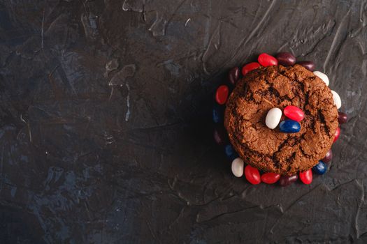 Homemade oat chocolate cookies stack with cereal with juicy jelly beans on textured dark black background, top view copy space