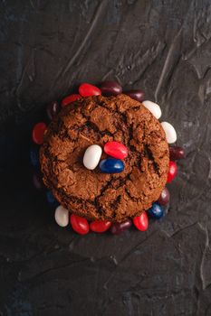 Homemade oat chocolate cookies stack with cereal with juicy jelly beans on textured dark black background, top view