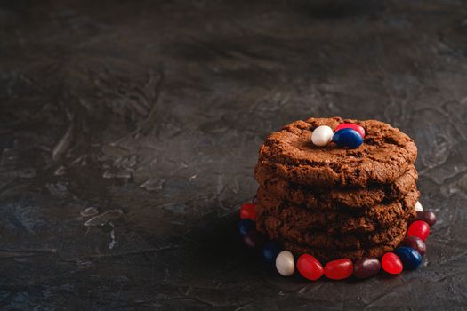 Homemade oat chocolate cookies stack with cereal with juicy jelly beans on textured dark black background, angle view copy space