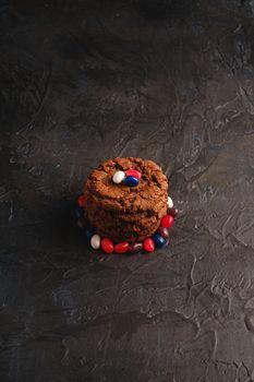 Homemade oat chocolate cookies stack with cereal with juicy jelly beans on textured dark black background, angle view