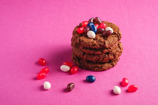 Homemade oat chocolate cookies stack with cereal with juicy jelly beans on minimal pink purple background, angle view