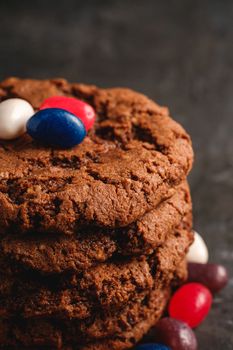 Homemade oat chocolate cookies stack with cereal with juicy jelly beans on textured dark black background, angle view macro