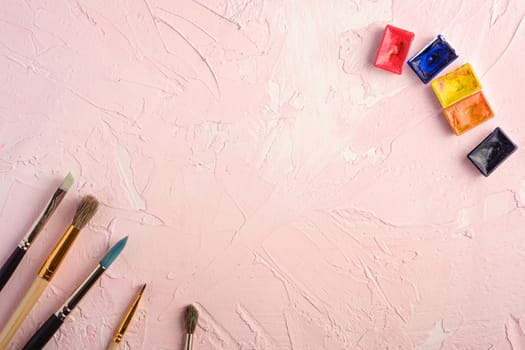 Paint brushes, artist tools for drawing on textured pink background, top view, copy space