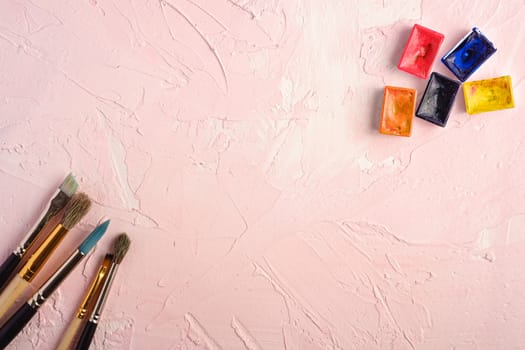 Paint brushes, artist tools for drawing on textured pink background, top view, copy space