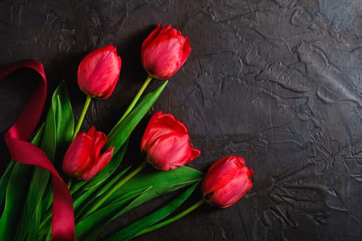 Red bunch of tulip flowers with red ribbon on textured black background, top view copy space