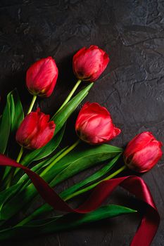 Red bunch of tulip flowers with red ribbon on textured black background, top view copy space