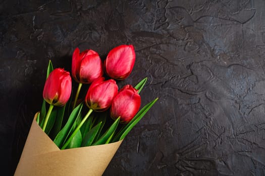 Bouquet of red tulip flowers on textured black background, top view copy space