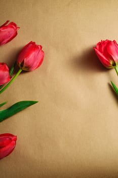 Bunch of red tulip flowers on textured brown paper background, top view copy space