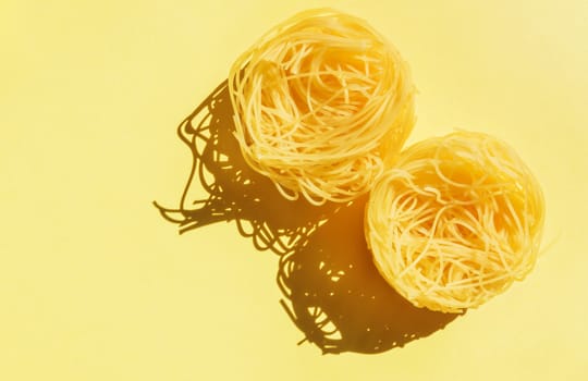 Dry Italian pasta called angel hair  on a yellow  background , two nests of yellow pasta ,funny composition , studio shot , top view