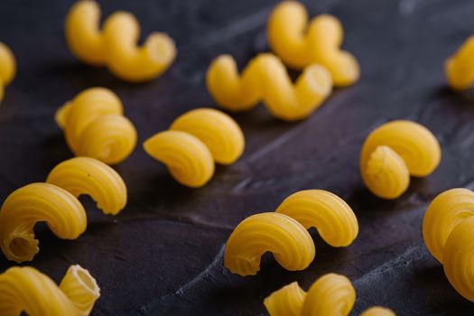 Scattered cavatappi uncooked golden wheat curly pasta on textured dark black background, angle view macro