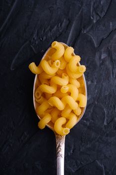 Cutlery spoon with cavatappi uncooked golden wheat curly pasta on dark textured background