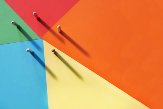 Five different colored pencils on a multicolored background, light shadow on the background .A horizontal and graphic composition,rainbow effect